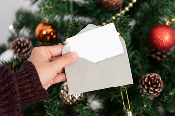 Hand holding mockup christmas greeting card for invitation design on christmas tree background.