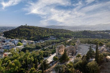 Panoramic view to the Odeon of Herodes Atticus (or Herodion) ancient greek theater as seen from the archaeological site of Acropolis. Filopappou hill in the background. Sunny day, cloudy sky