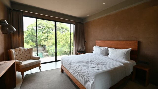 Modern tropical bedroom with wooden furniture, sofa and swimming pool view from balcony in the resort