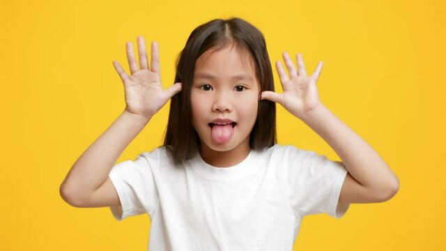 Funny Little Korean Girl Sticking Out Tongue Grimacing, Yellow Background