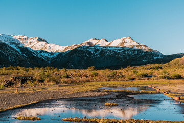 Fototapeta premium montañas nevadas reflejos en el agua , hora dorada al atardecer, coloreas azul y verdes 