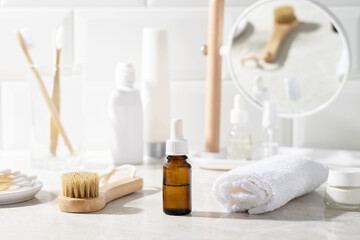 Massage oil or facial serum in a glass bottle in the bathroom. White towel, cream, toothbrushes in...