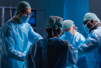 Multiracial team of professional medical surgeons performs the surgical operation in a modern...