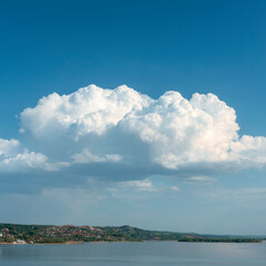 Fototapeta na wymiar group of white cumulus clouds on blue sky over hilly river bank as natural background