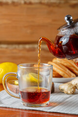 Strong saturated tea is poured into a cup from a glass teapot next to lemon and ginger.