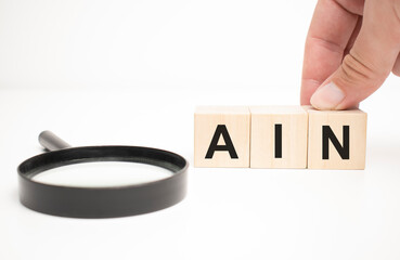 ain text wooden cube blocks and hand holding magnifying glass on table background.
