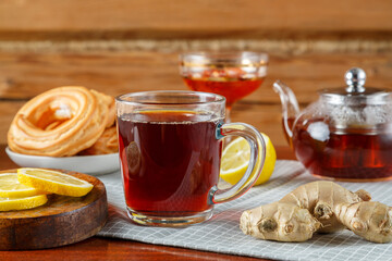 On the table is a cup of strong tea with lemon and ginger, donuts and jam in a vase.