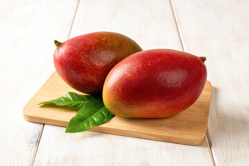 Two red ripe Palmer mangoes on a cutting board over white wooden table. Ready to eat whole sweet...