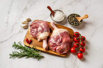 Two fresh raw duck legs on a wooden cutting board and salt, pepper, garlic, green rosemary and red...