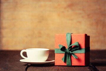 Cup of coffee and gift box on wooden table.