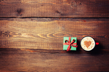 Cup of coffee and heart shape next to gift box on wooden table.