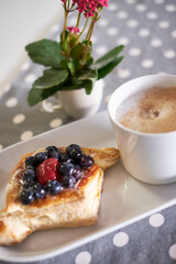 Cappuccino coffee and fruit pastry in front of a small table plant (vertical)