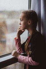 A beautiful young girl looks out the window with rain and dreams. Rain. Autumn. Atmosphere.