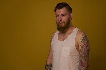 bearded man in white t-shirt with tattoos on his arms posing serious look