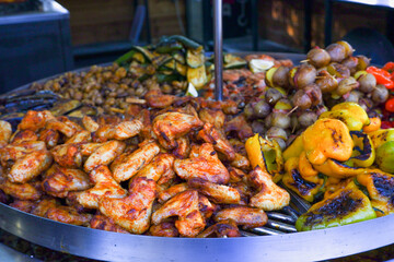 Street food. Assorted food grilled on a stainless steel turntable. Sausages, meat, corn, grilled vegetables. A slide of food. Large assortment of food grilling on a barbecue