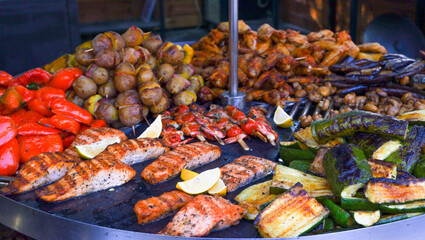 Street food. Assorted food grilled on a stainless steel turntable. Sausages, meat, corn, grilled vegetables. A slide of food. Large assortment of food grilling on a barbecue