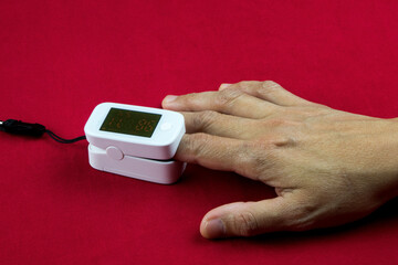 Finger Inserted in Medical Oxygen Monitoring Meter on a Red Table Surface