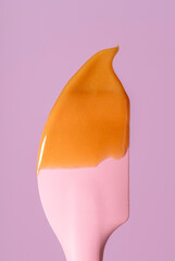 Caramel sauce dripping on a silicon spatula, minimalist on a pink background.