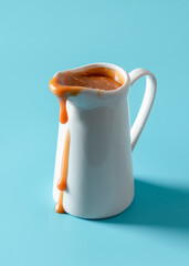 Caramel jug isolated on a blue background. Caramel sauce dripping