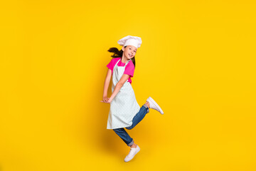 Photo of positive dream small girl jump hold hands wear apron cap footwear isolated yellow color background