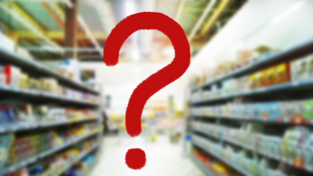 Large red question mark on abstract blur image of supermarket background. Defocused shelves with products. Grocery shopping. Store. Retail industry. Inflation and problem concept. Business and finance