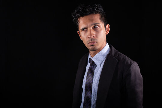 Businessman suspicious of something he looks askance at. Young latin with suspicious look and expression, looking for something. Isolated on a black background.