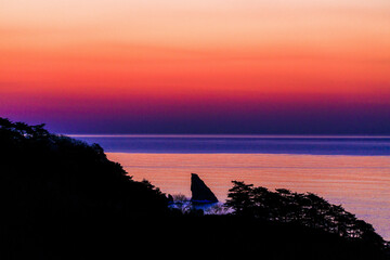 Far Eastern Marine Reserve. A sharp rock sticks out of the sea against the backdrop of a glow. Dawn in the Sea of Japan. Rocky coast in the south of the Far East.