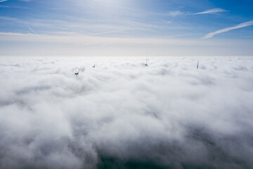 Wind farms sticking out above the clouds, aerial view of distant turbine propellers