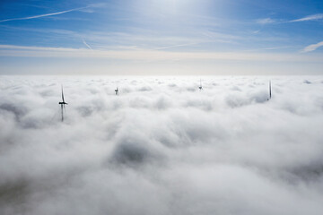Fototapeta premium Wind farms sticking out above the clouds, aerial view of distant turbine propellers