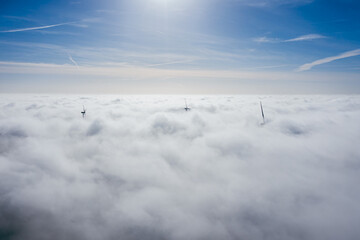 Wind farms sticking out above the clouds, aerial view of distant turbine propellers