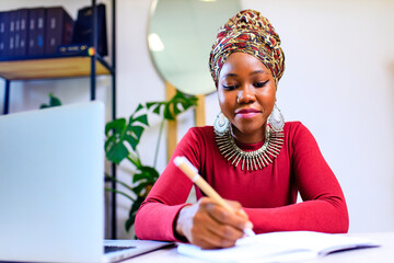 Image of african american woman with turban over head using laptop in office