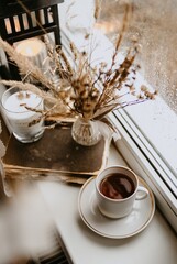 coffee cup and dry brown flowers on the window