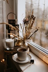 coffee cup and dry brown flowers on the window