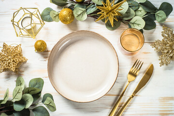 Christmas table setting with eucalyptus leaves and luxury metallic golden decorations. Top view at...
