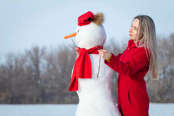 Attractive woman in red coat making big snowman