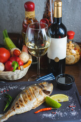 Grilled fish on a plate with a glass of wine and baked vegetables.