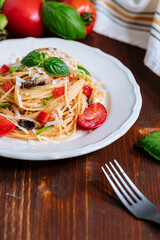 Fresh pasta with spaghetti, tomato, mushrooms, basil and parmesan cheese in white plate on a wooden background with ingredients in background