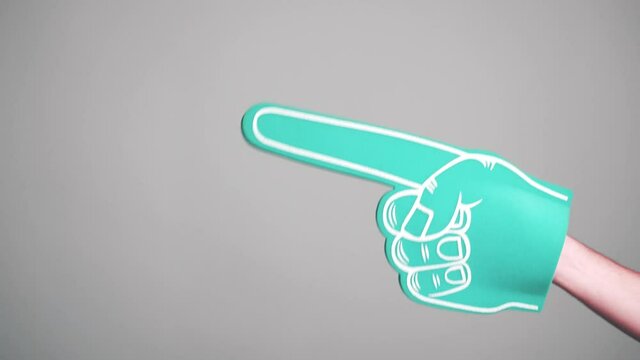 Footage of pointing with foam finger glove at copyspace over grey background.