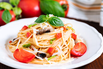 Fresh pasta with spaghetti, tomato, mushrooms, basil and parmesan cheese in white plate on a wooden background with ingredients in background