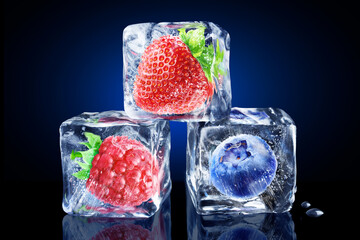 A pyramid of three ice cubes with berries inside on a dark blue background. Raspberry, strawberry,...