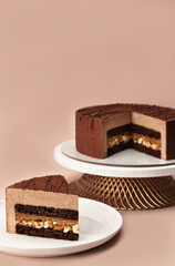 Delicious chocolate mousse cake on a stand and slice with the layers and texture displayed on pastel coffee colored background. Restaurant menu and confectionery concept. Close-up. Copy space.