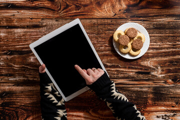 Woman's hands holding digital tablet and eating cookies on the wooden table