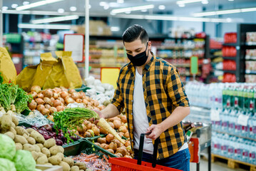 Young handsome man in a supermarket wearing protective mask while grocery shopping