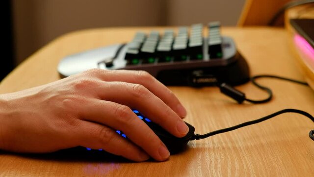 Controlling the game using a modern gaming rgb mouse and a mini keypad. A man plays with two hands on new equipment.