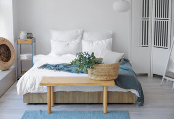 Basket with green eucalyptus branches on bench in bedroom