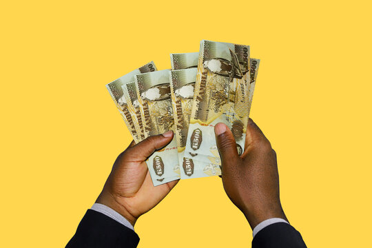 Black Hands in suit holding 3D rendered Zambian Kwacha notes over yellow background