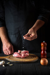 The cook sprinkles the meat with salt. Preparing meat before baking. Working environment in restaurant kitchen