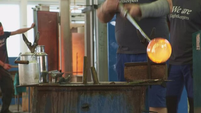 Glass blower produces a handmade glass bottles or vase. Glassworks manufacturing process 
