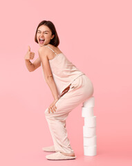 Young woman with many rolls of toilet paper showing thumb-up on color background