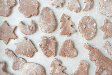 Top view of white tefon baking paper full of Christmas shaped gingerbread cookies ready for the oven.